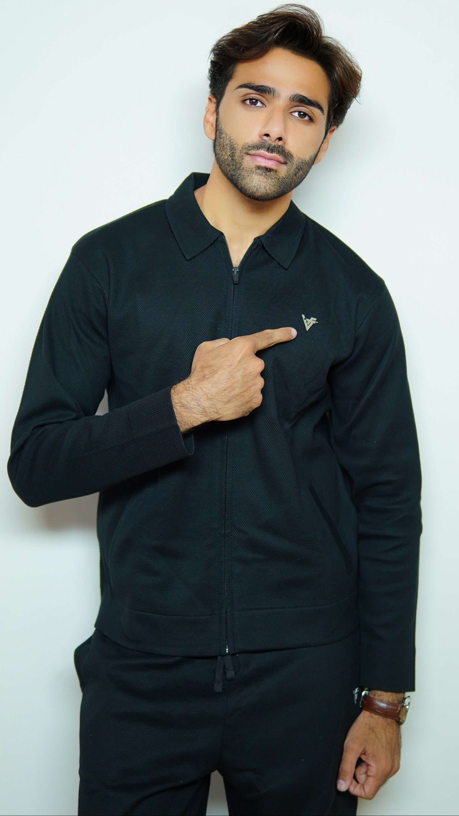 Man wearing a black jacket pointing at himself against a white background