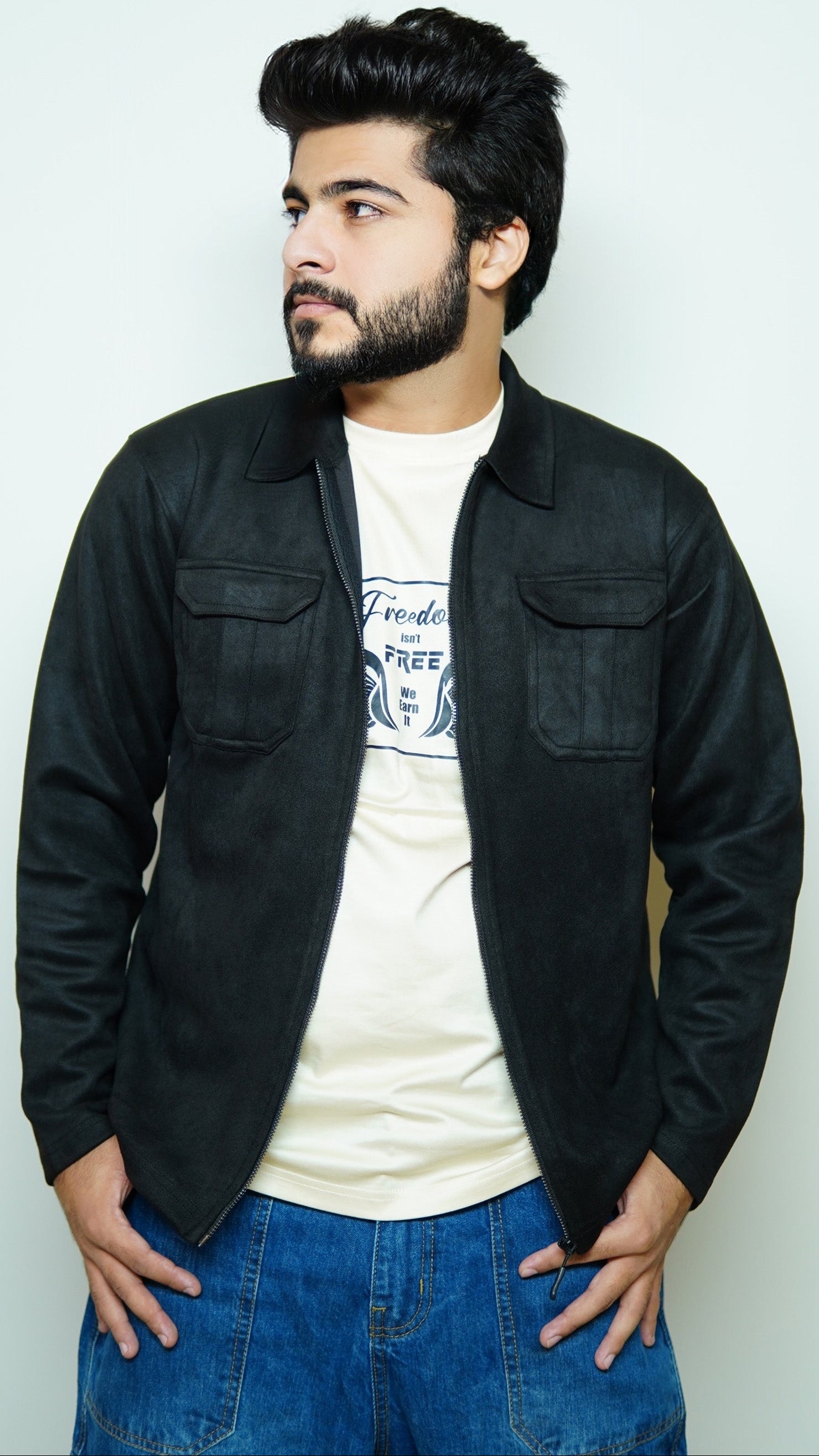 Man wearing a black jacket over a white shirt with blue jeans against a light background