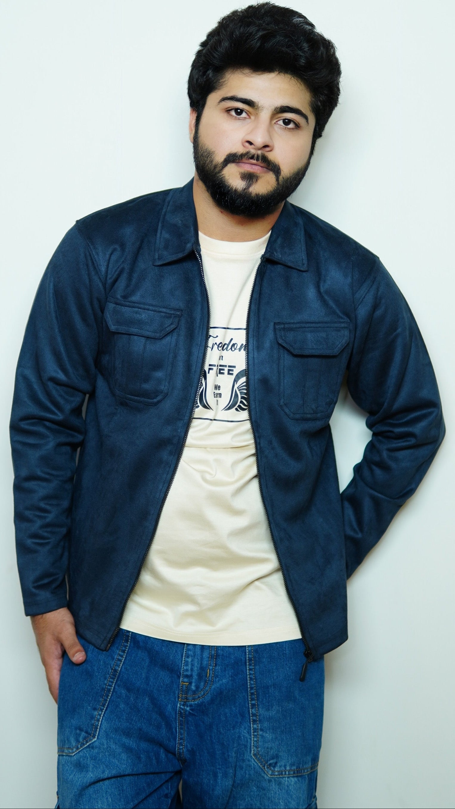 Man wearing a blue jacket over a white shirt with text, standing against a light gray background