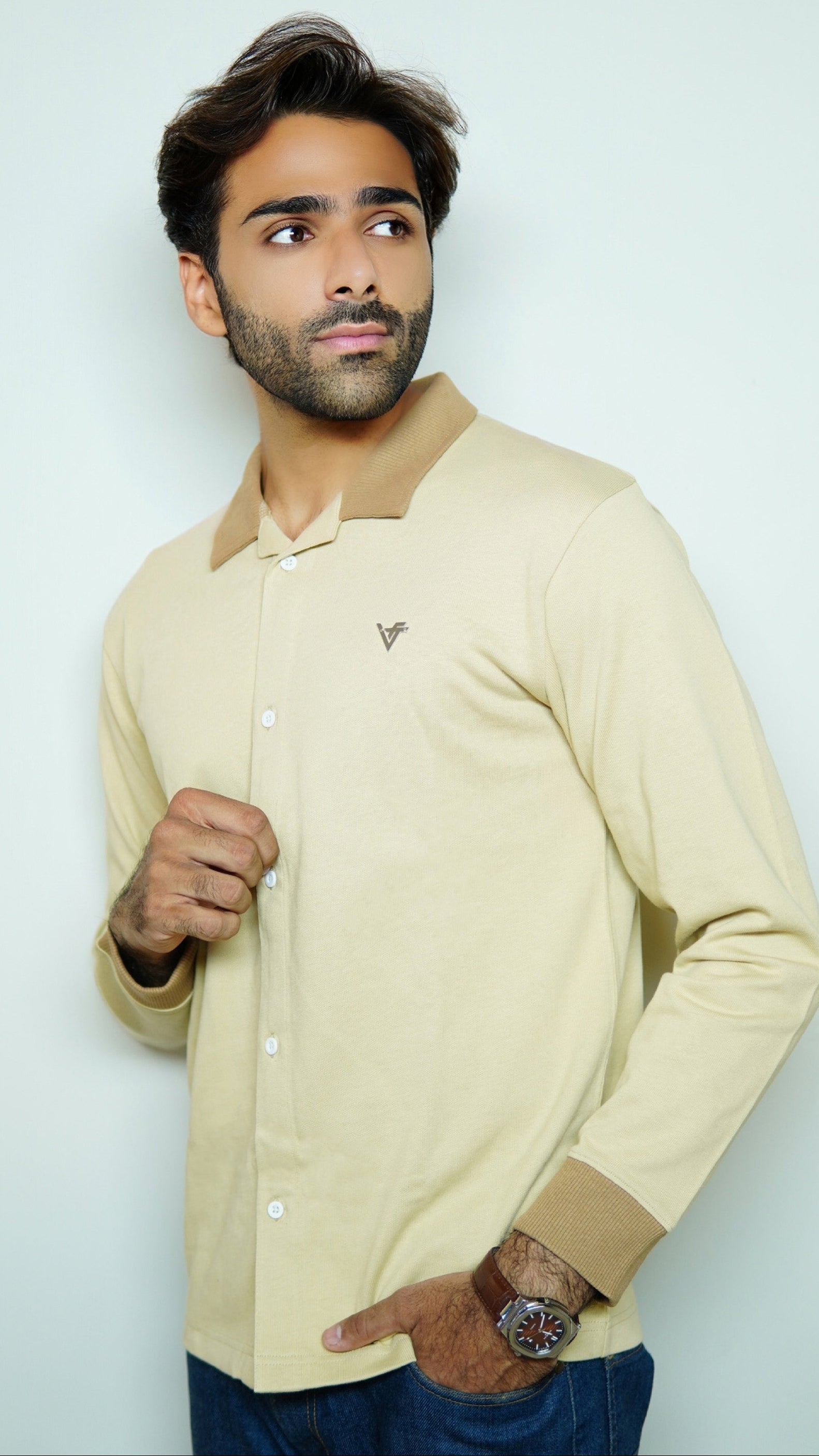 Man wearing a beige shirt with a small logo on a light gray background