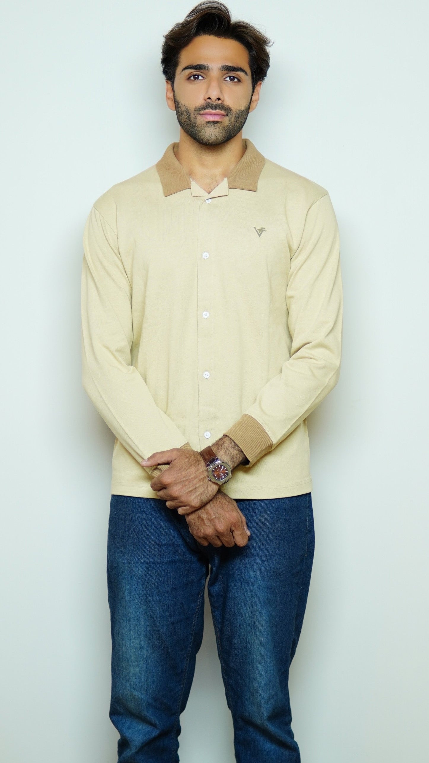 Man wearing a light-colored sweater with a collar and blue jeans against a white background