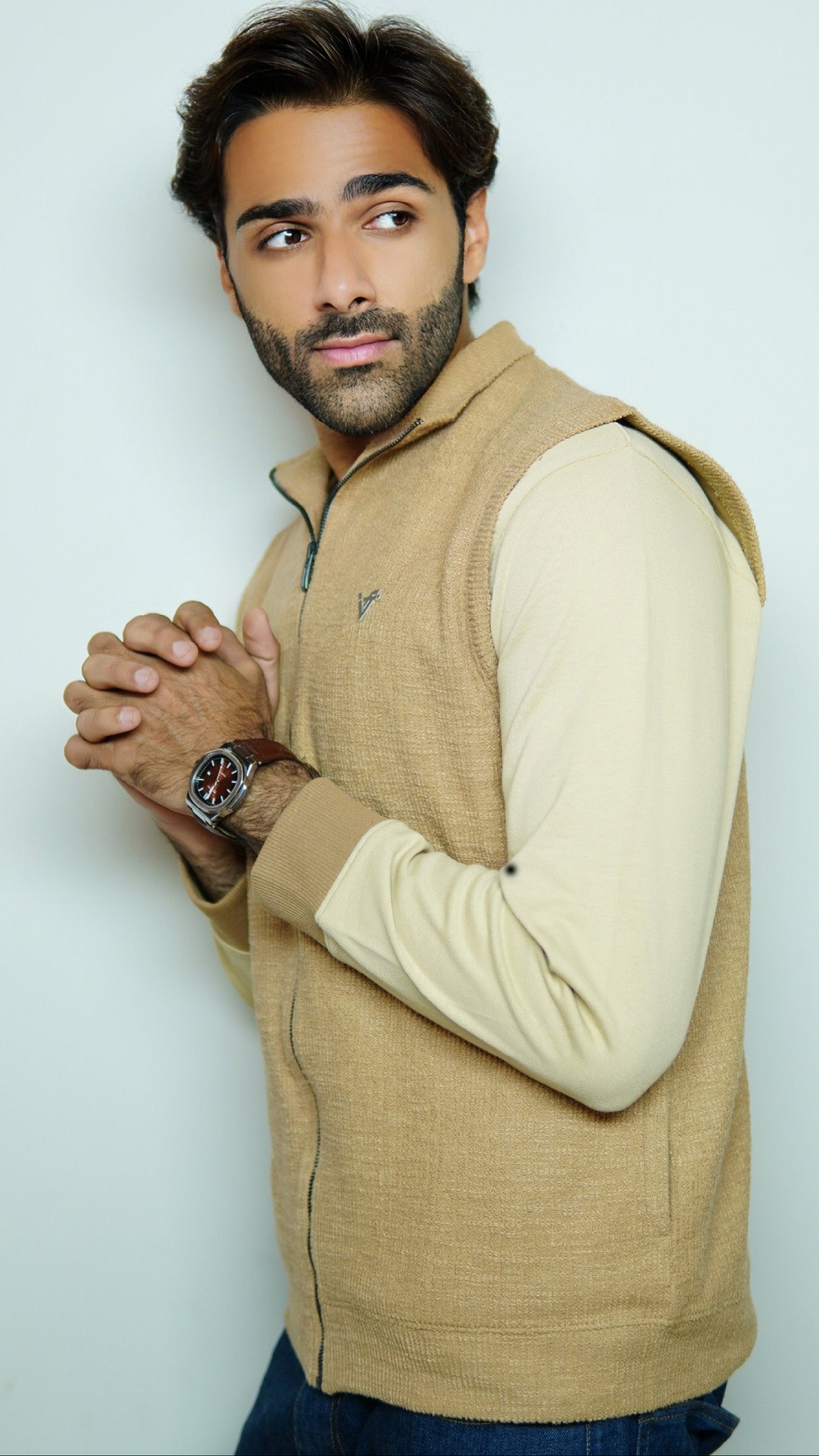 Man wearing a beige vest over a white shirt against a light background
