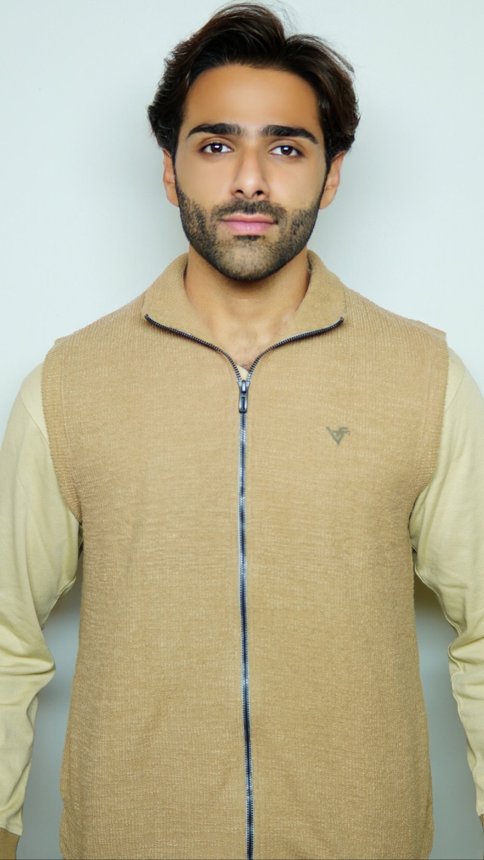 Man wearing a beige vest over a light shirt against a plain background