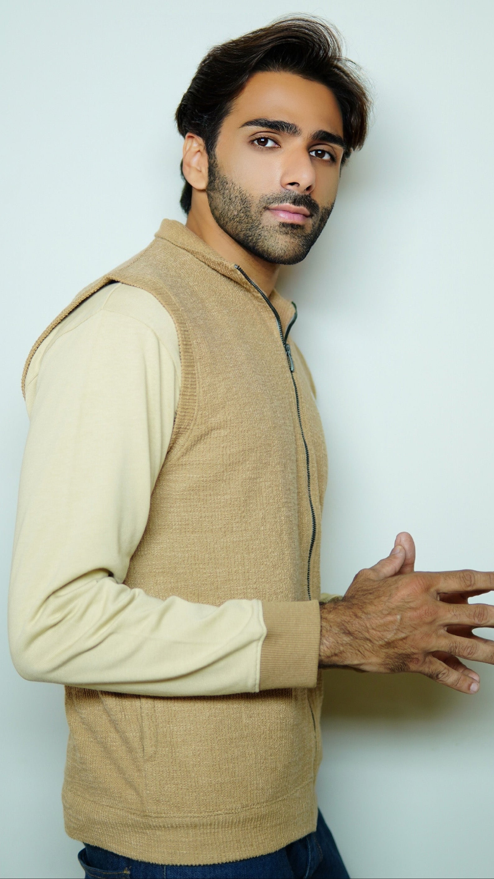 Man wearing a beige vest over a white shirt against a light gray background