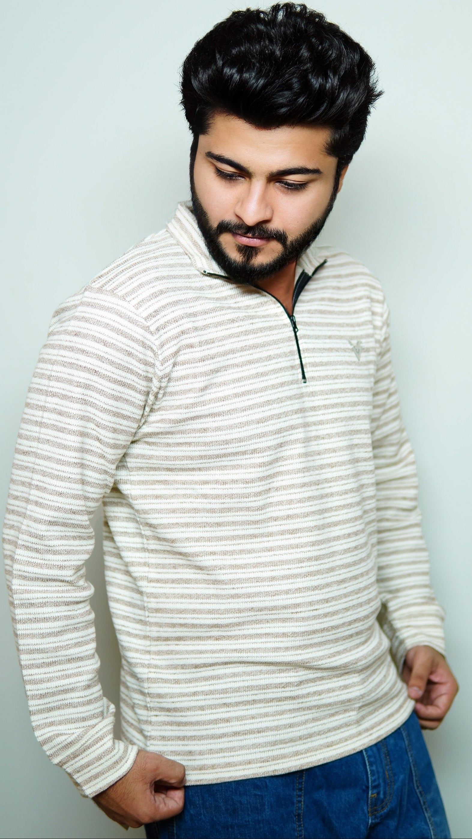 Man wearing a striped sweater and blue jeans against a light background