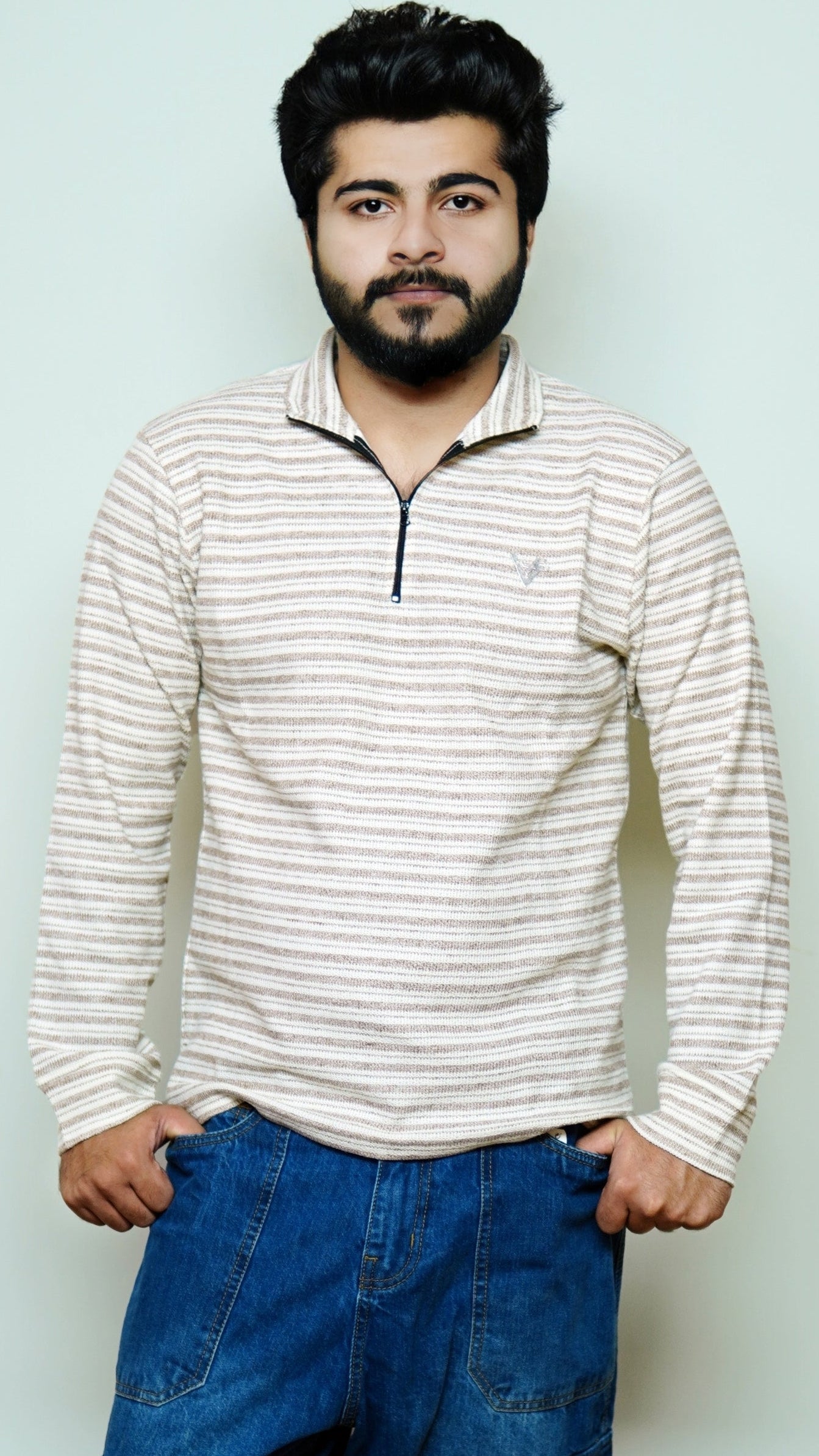 Man wearing a striped long-sleeve shirt and blue jeans against a light background