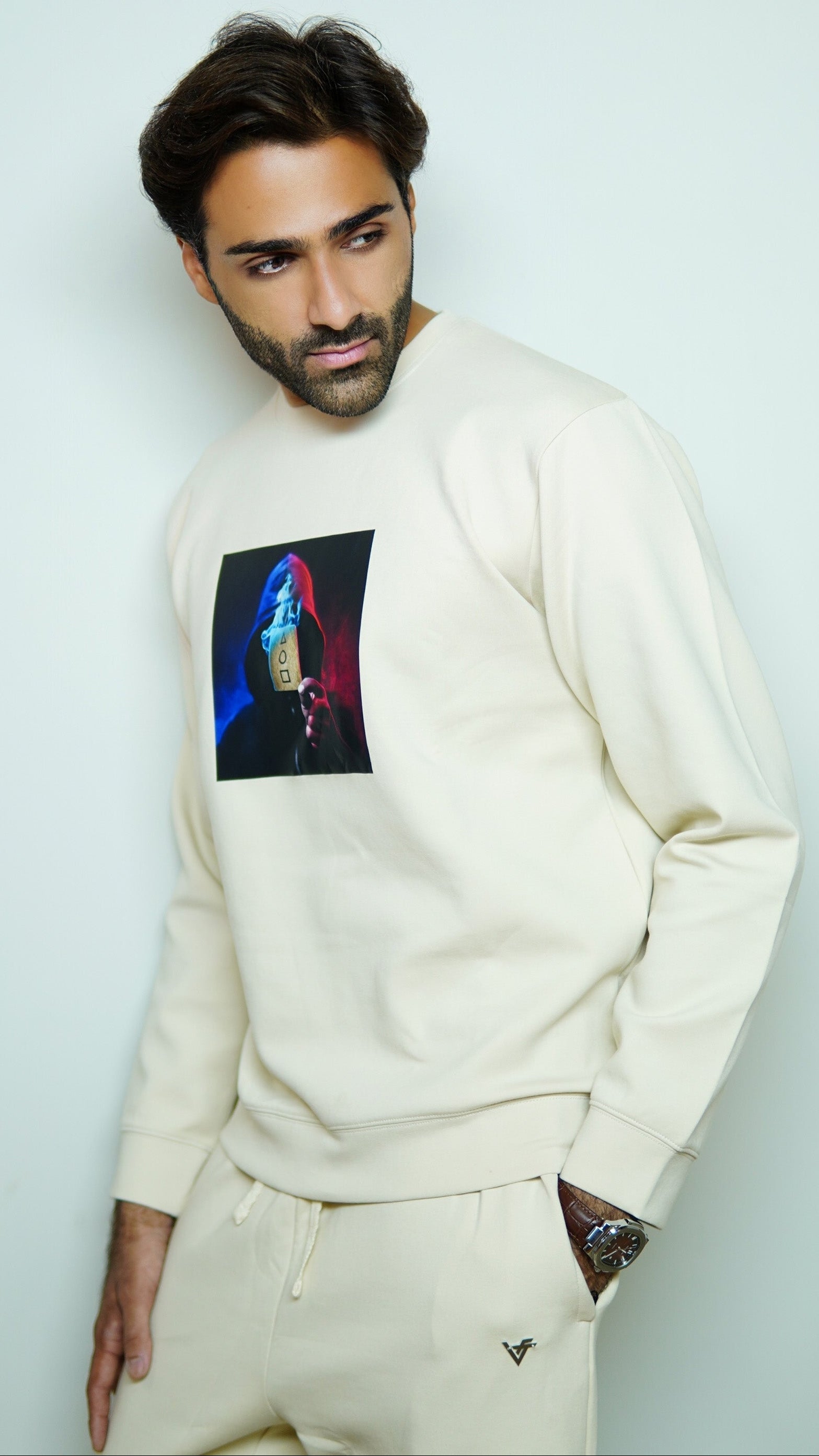 Man wearing a cream sweatshirt with a colorful graphic design on a light gray background