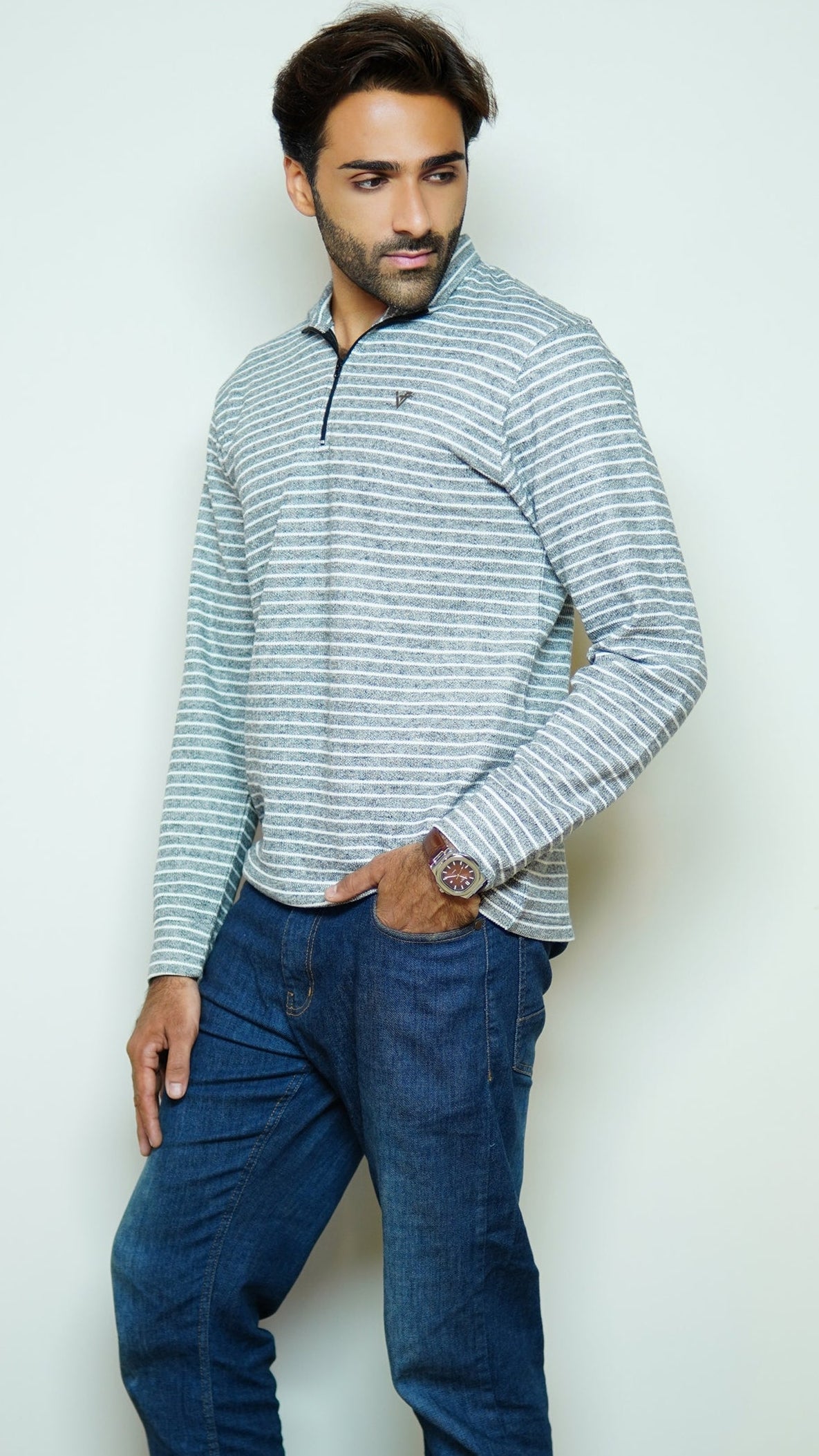 Man wearing a striped sweater and blue jeans against a plain background