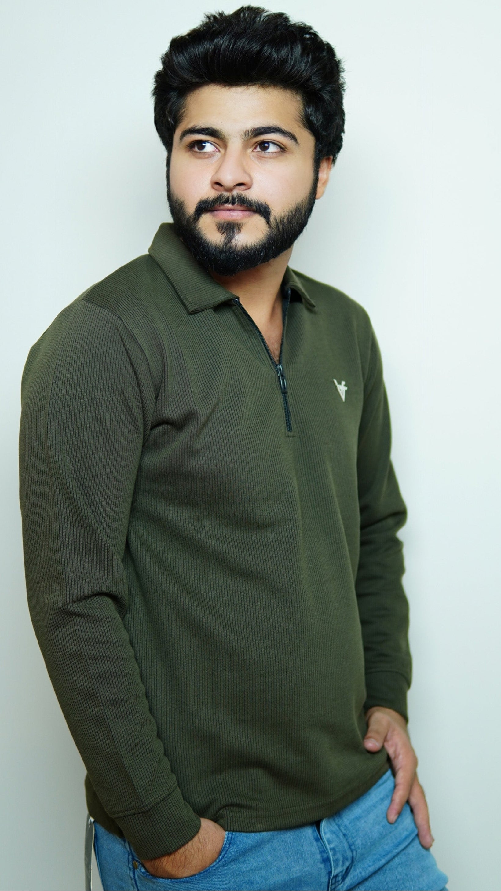 Man wearing a green long-sleeve shirt and blue jeans against a white background