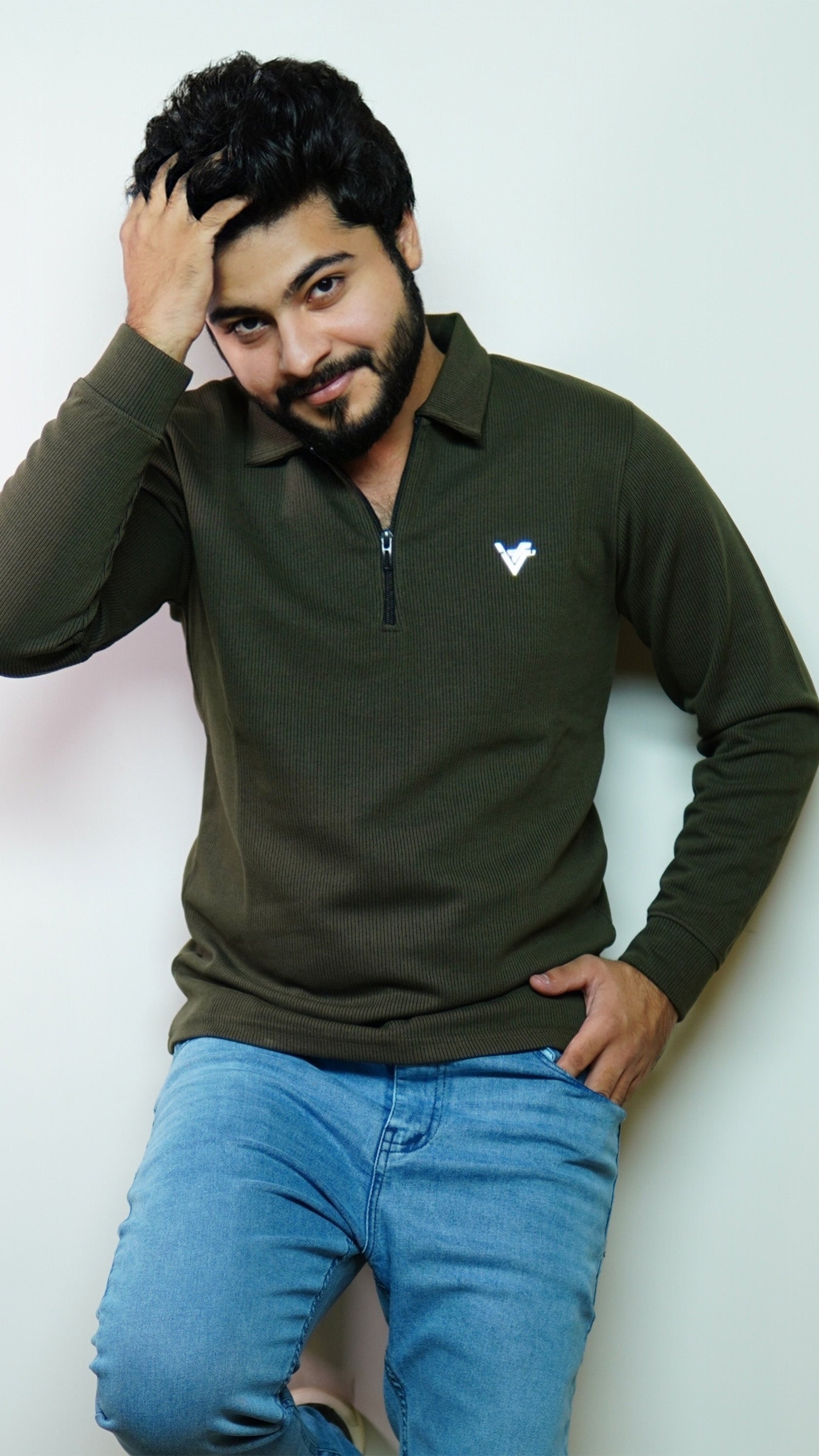 Man wearing a green long-sleeve shirt with a logo and blue jeans against a white background