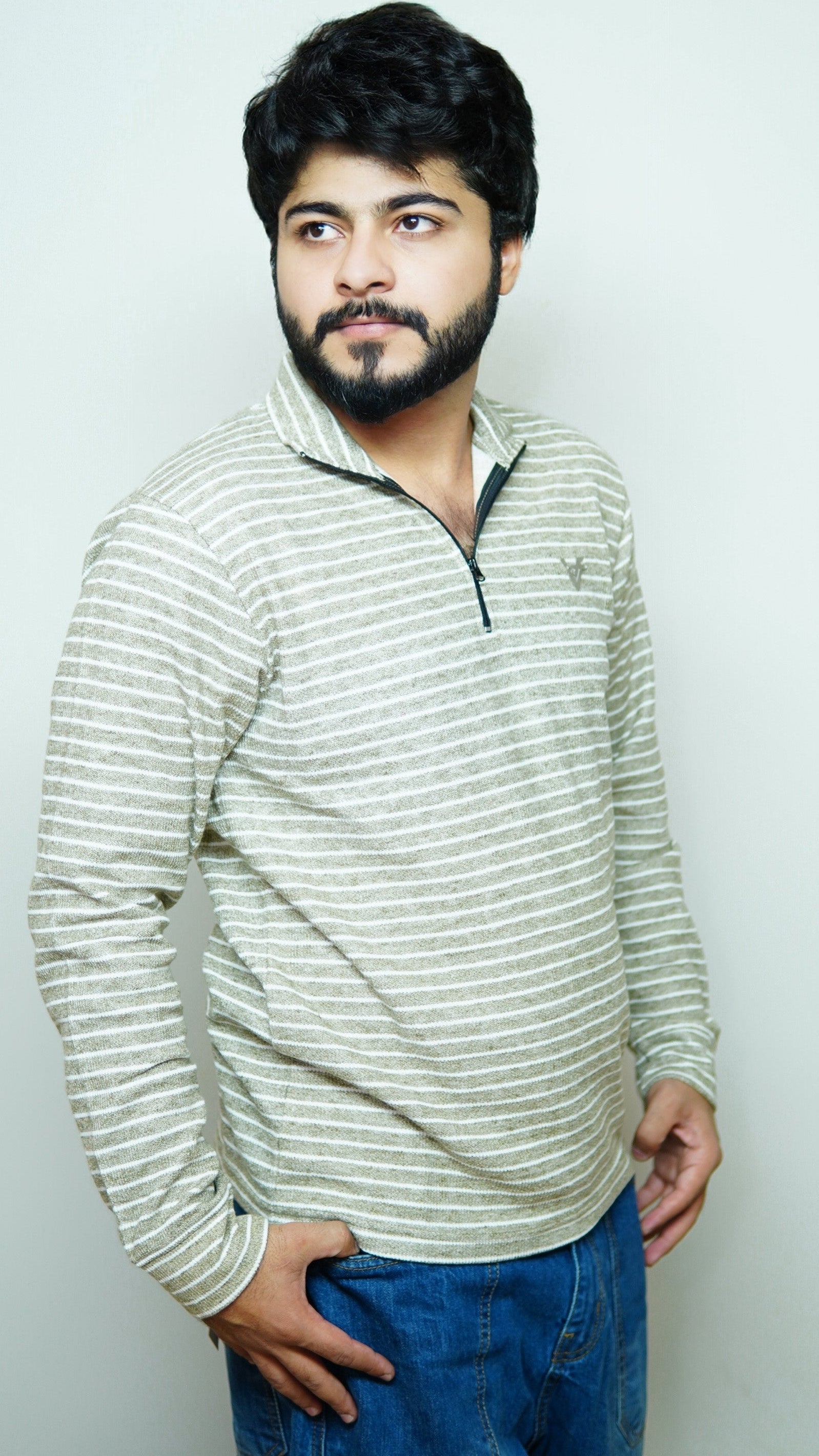Man wearing a striped sweater and blue jeans against a plain background