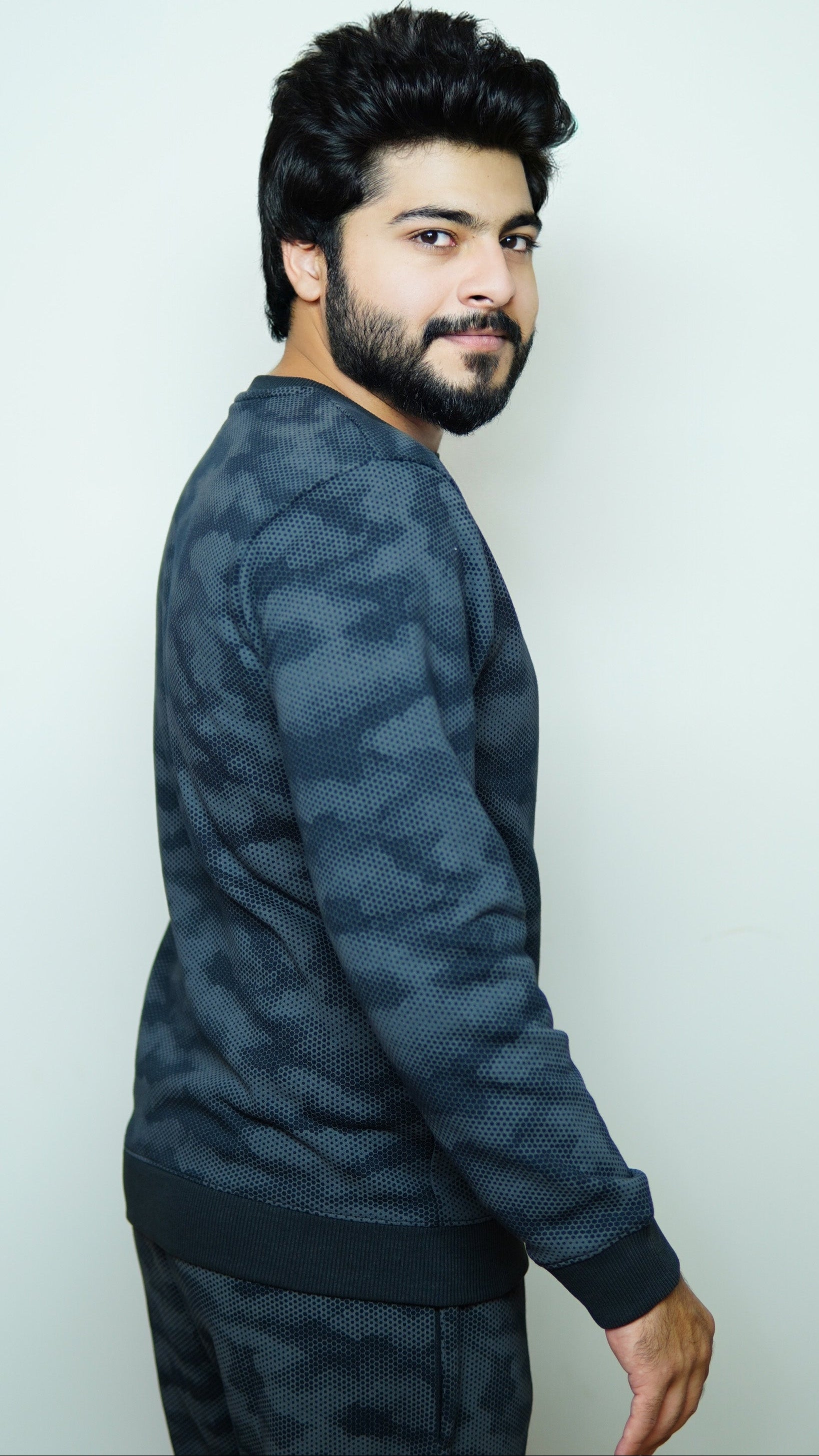 Man wearing a dark blue camouflage-patterned sweater against a white background