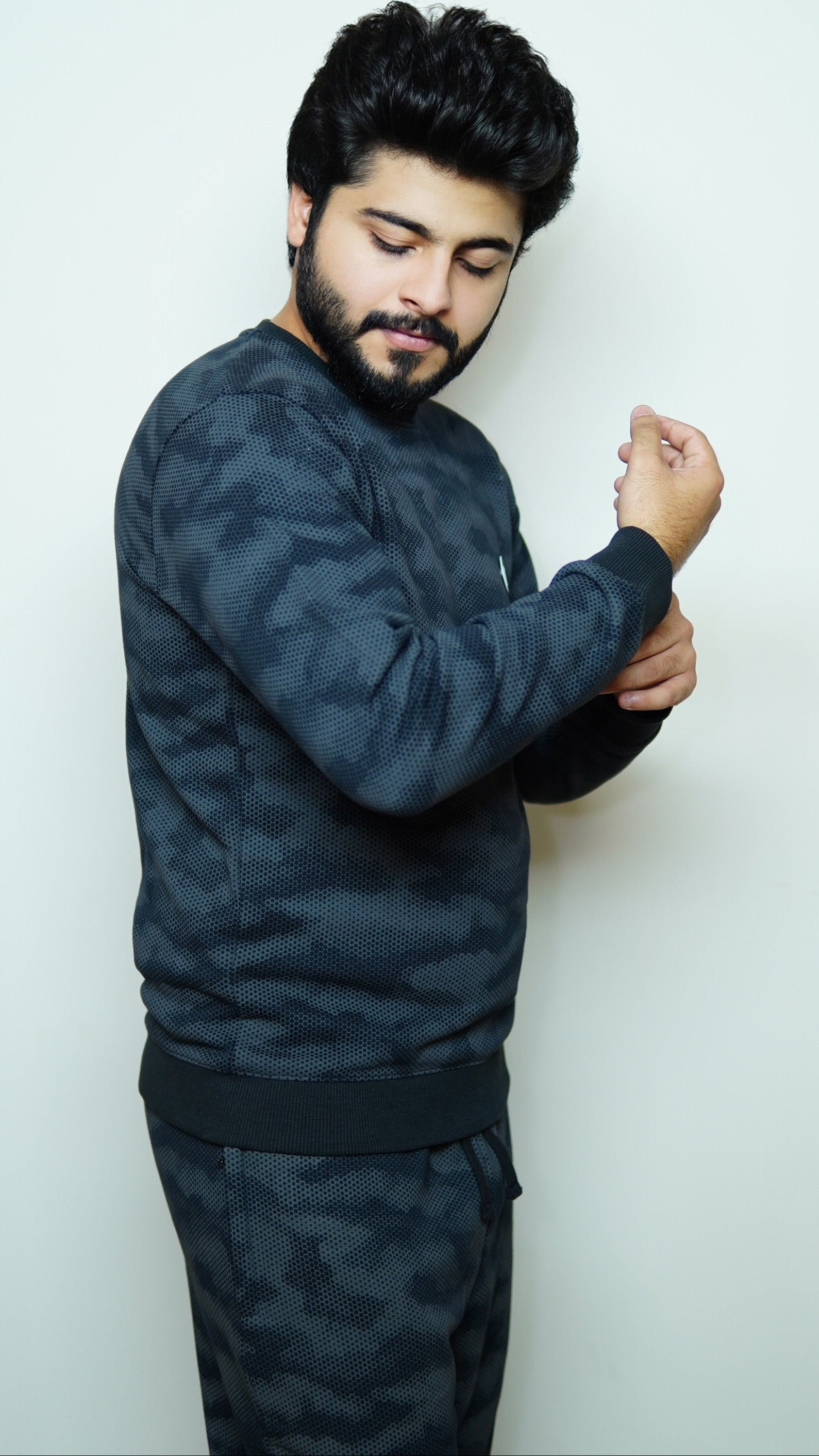 Man wearing a dark camouflage outfit against a white background