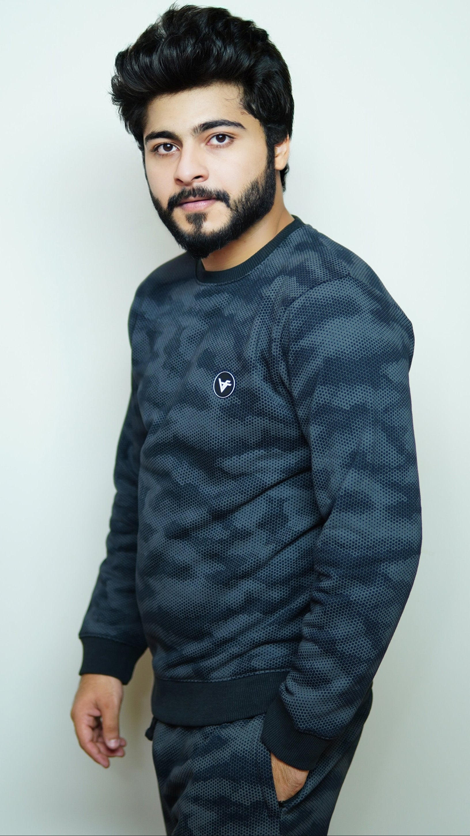 Man wearing a dark camouflage sweater and pants against a light background