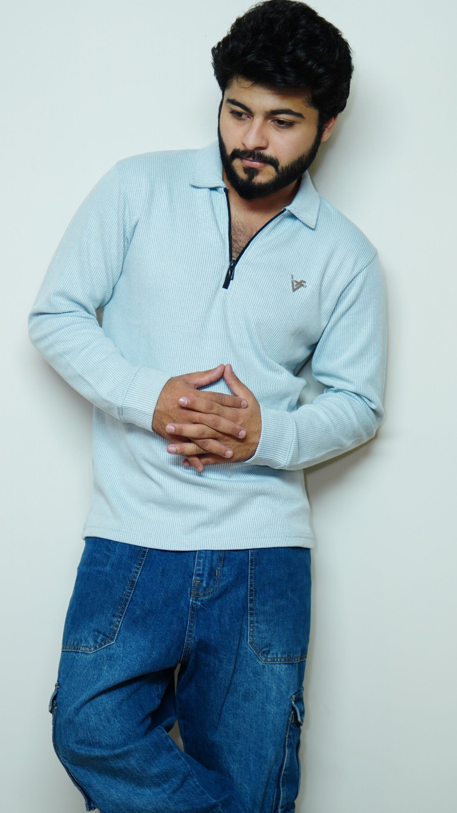 Man wearing a light blue sweater and blue jeans against a white background