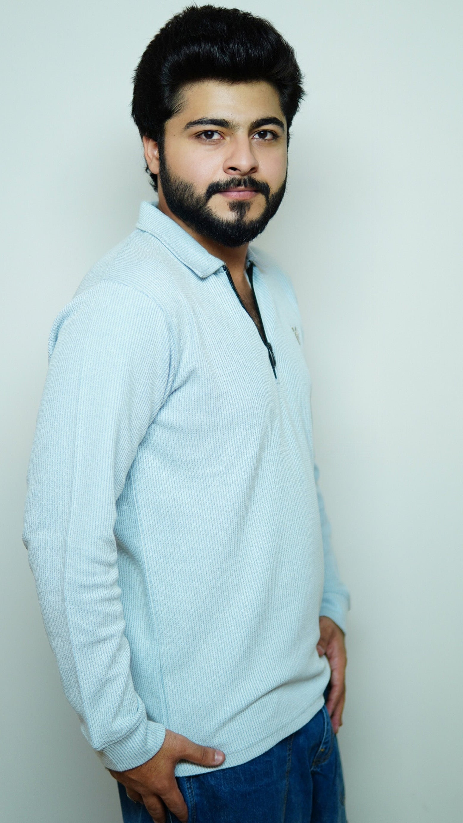 Man wearing a light blue sweater and dark pants against a plain background